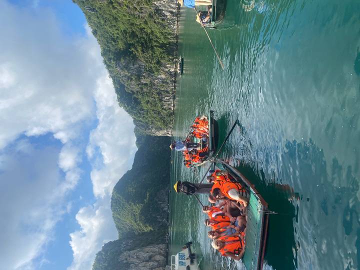 Groups in orange vests row traditional boats between limestone karsts on emerald bay waters.