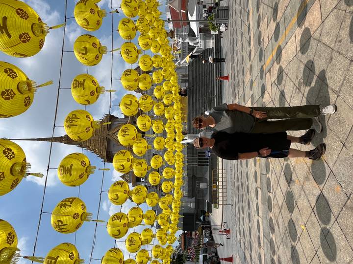 Travellers standing beneath rows of bright yellow lanterns in front of an ornate Thai temple.