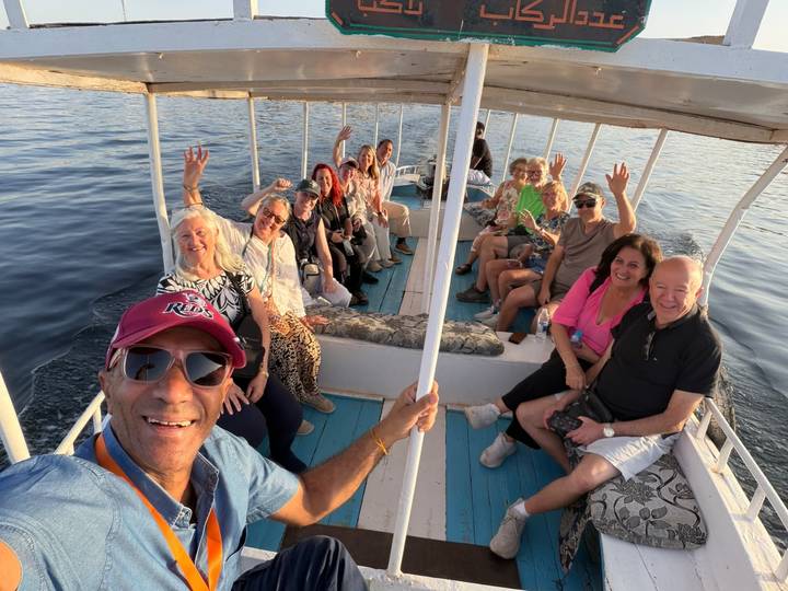 Cheerful tour group waves from an open boat cruising on calm Nile waters during golden afternoon light.