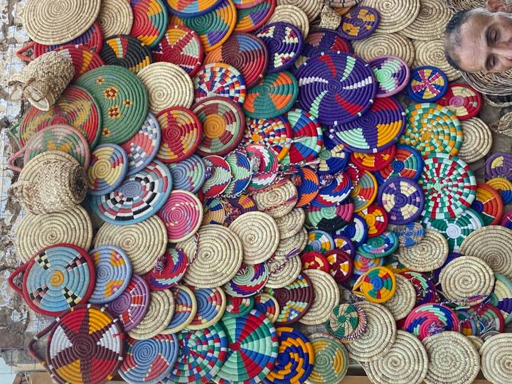 A vibrant wall display of colorful woven straw plates and baskets at a market stall.