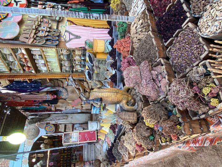 A spice and souvenir stall packed with colorful herbs, jars, fabrics and a carved crocodile figurine.