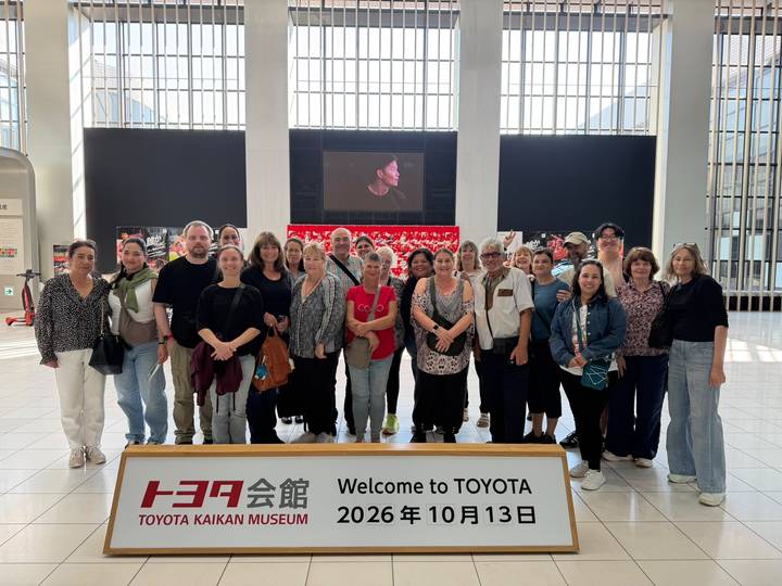Large tour group posing inside Toyota museum lobby with bilingual welcome sign.
