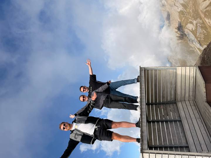 Three friends pose with arms outstretched on a mountaintop viewing deck above the clouds.