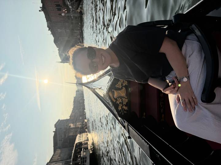Woman enjoying a gondola ride on a Venetian canal at sunset with golden light reflecting on the water.