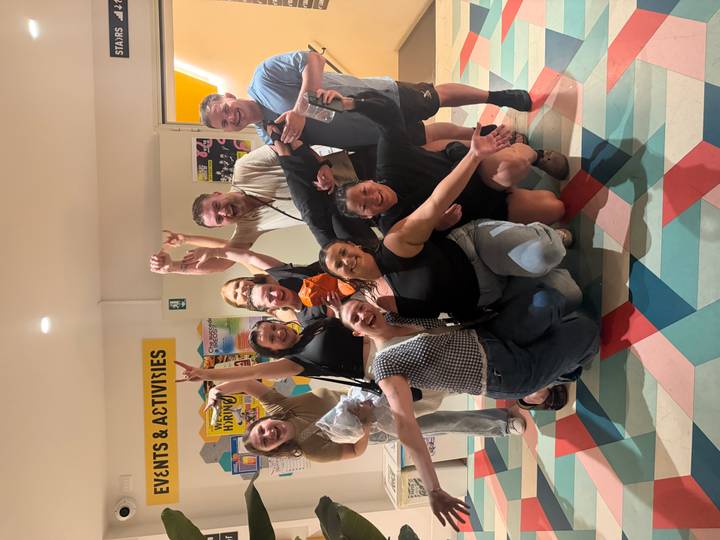 Cheerful group posing inside a hostel lobby area, arms raised in celebration.
