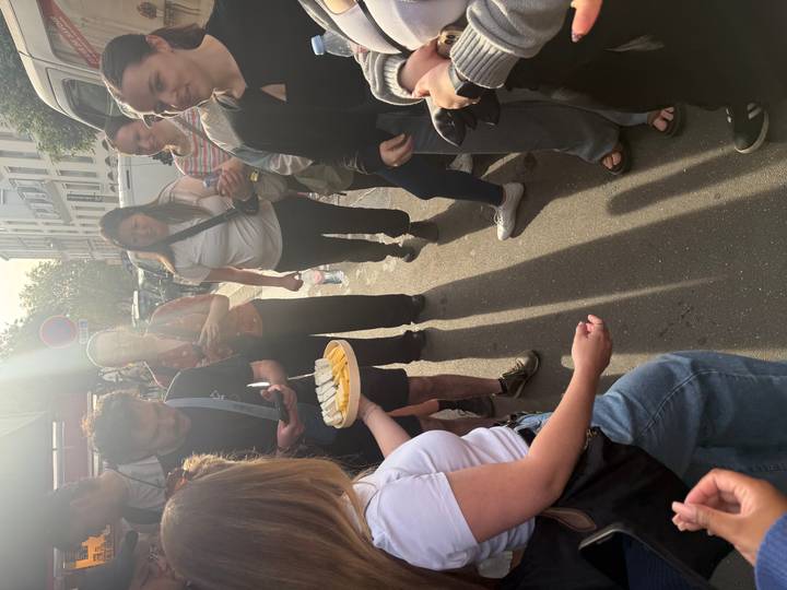 Group gathered on a Parisian street sampling cheese under bright afternoon sun.
