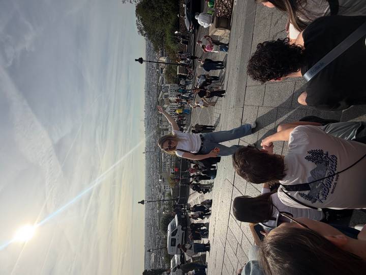 Local guide gesturing over the panoramic view of Paris from the steps of Sacré-Cœur with city skyline below.