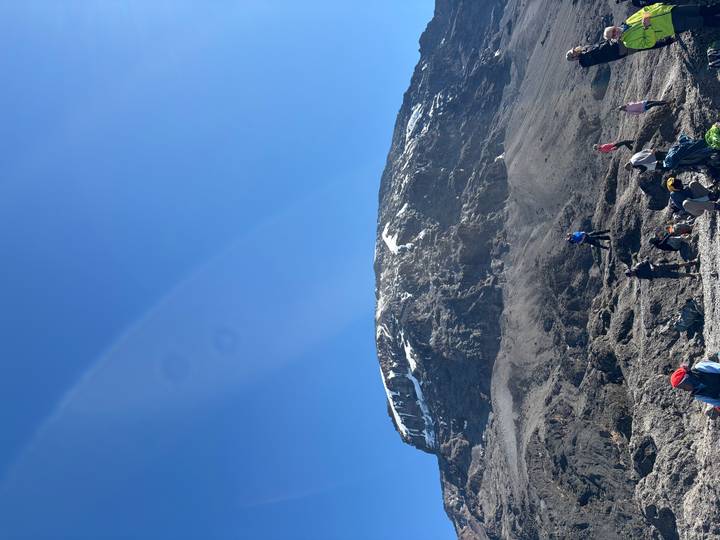 Trekkers rest at the base of Kilimanjaro’s snowy crater under a vivid blue sky.