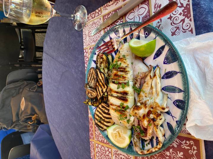 Plate of grilled seafood and vegetables garnished with lime on a patterned tablecloth.