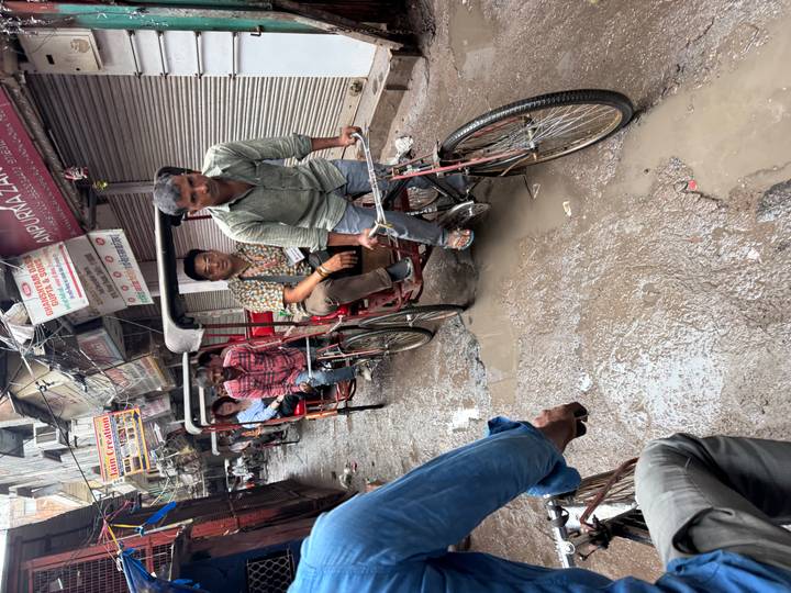 Cycle rickshaw drivers pull passengers through a narrow, wet alley lined with shuttered shops.