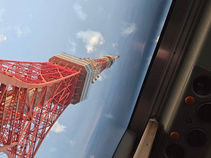 A tilted upward view of the red lattice Tokyo Tower set against a blue sky scattered with clouds.
