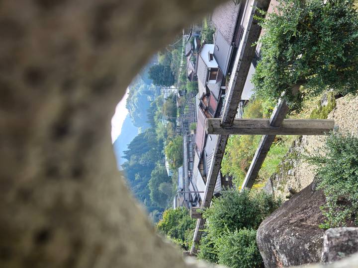 A framed view through stone shows a quiet Japanese mountain village nestled among forested hills.