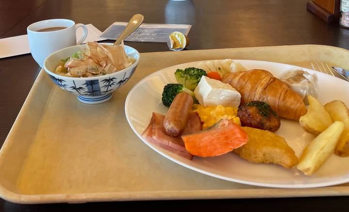 Cafeteria breakfast tray with assorted western and Japanese dishes beside a cup of coffee.