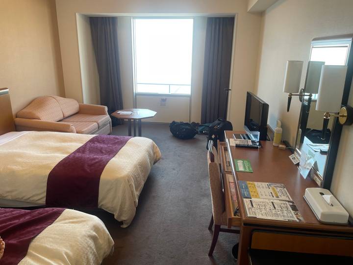 Neat hotel room with twin beds, sofa, desk and large bright window.