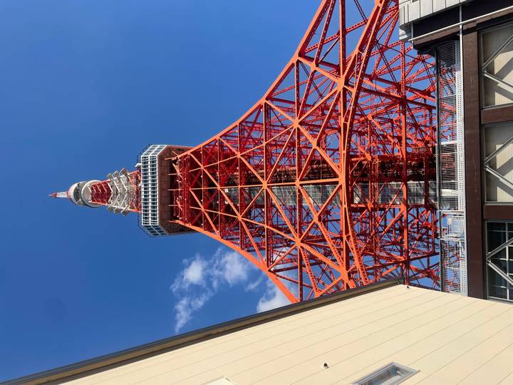 Looking up at the bright red lattice of Tokyo Tower set against a deep blue sky.