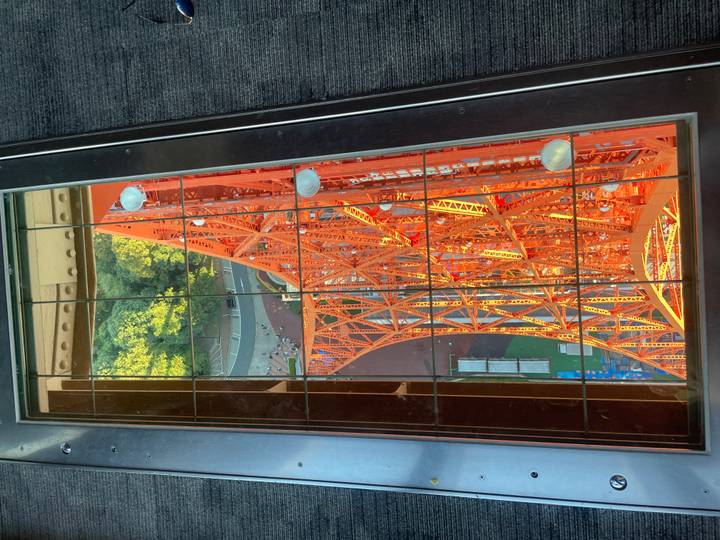 View through a glass floor down the vivid orange steel lattice of Tokyo Tower.