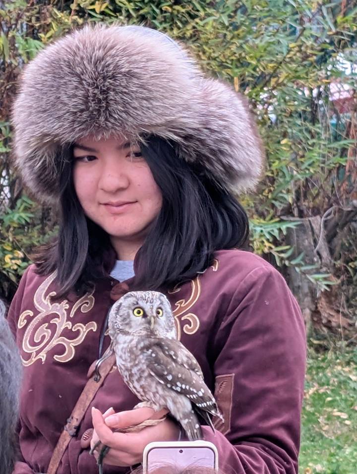 Portrait of a woman in a fur hat and embroidered coat holding a small owl.