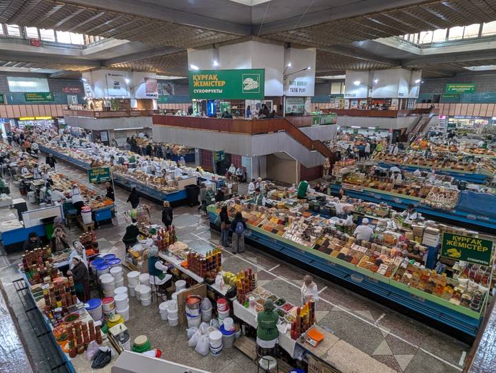 Bustling indoor food market hall with rows of produce stalls and shoppers.