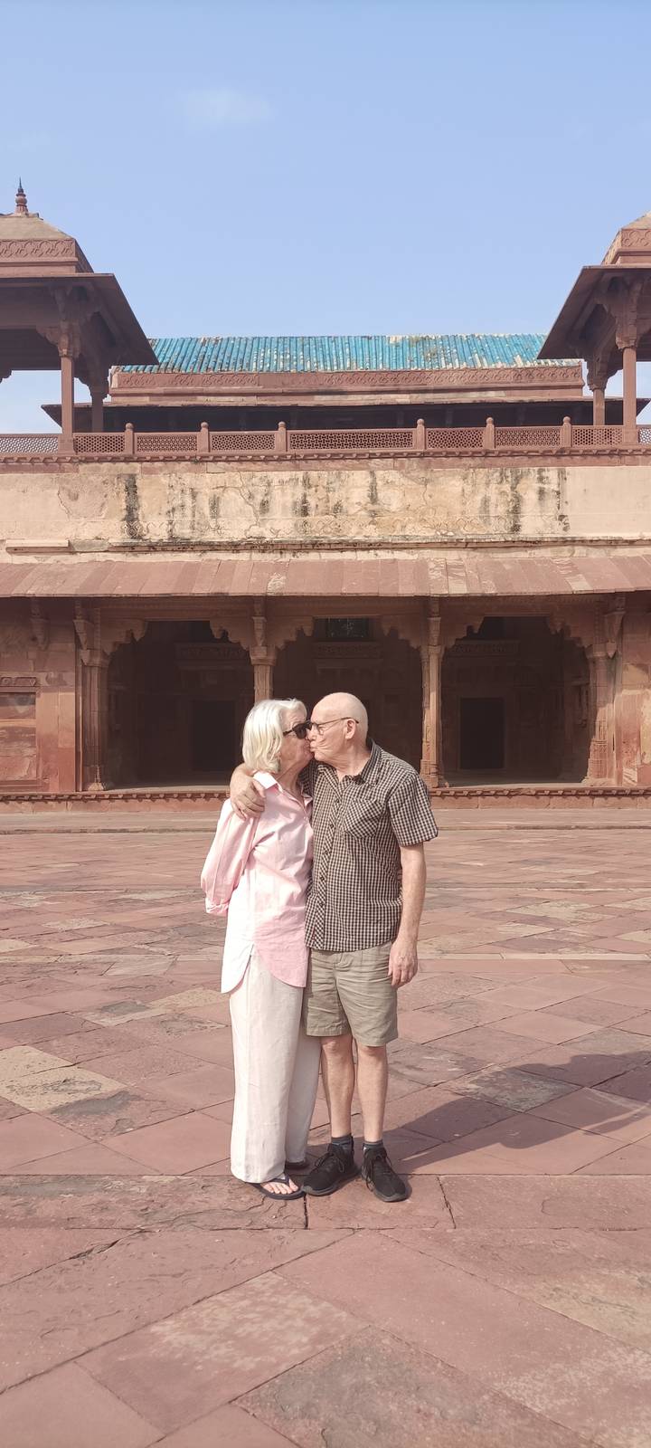 Couple kiss affectionately in front of red sandstone arches at Fatehpur Sikri.