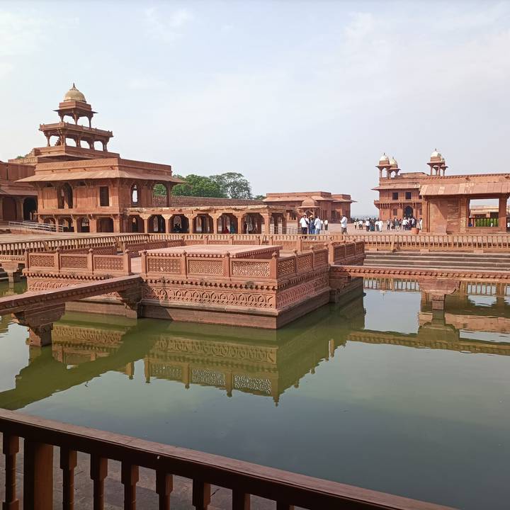 Intricate red sandstone pavilions and water pools of Fatehpur Sikri reflected in green water.
