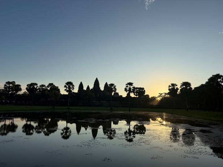 Silhouetted towers of Angkor Wat reflect in a lotus pond at sunrise with the first golden light.