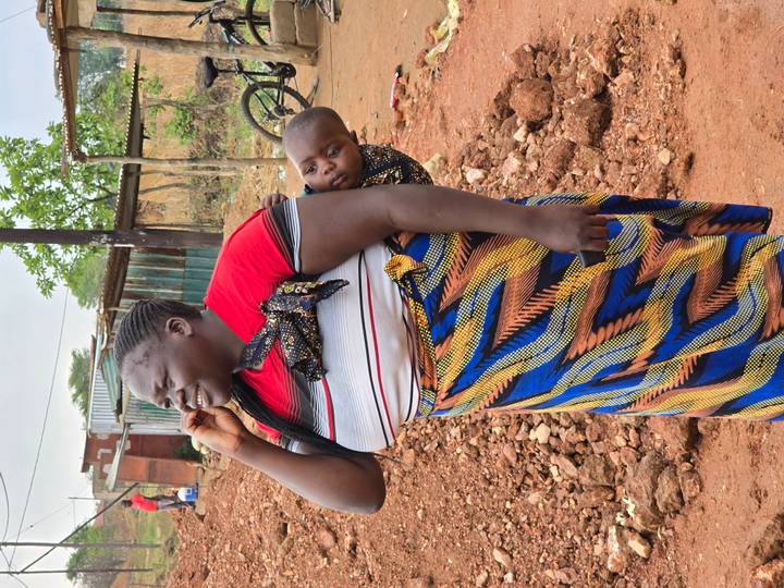 Woman in colorful skirt carries a small child on her back while speaking on a phone.