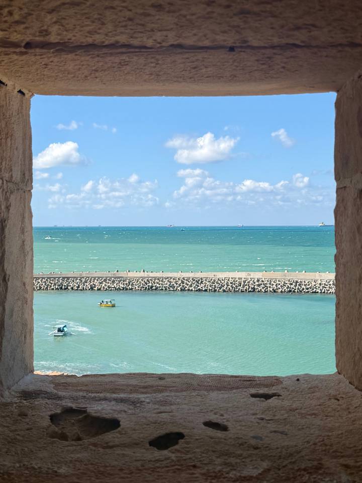 Turquoise Mediterranean waters and small boats framed by sandstone battlement window.