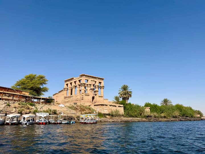 Ancient Philae temple with grand stone columns rising above the Nile as small boats bob alongside.