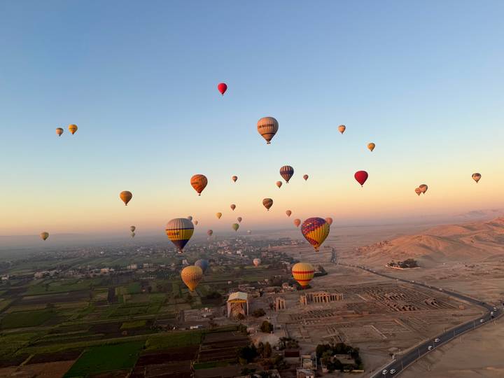 Dozens of colourful hot-air balloons float above temples and farmland of Luxor at dawn.