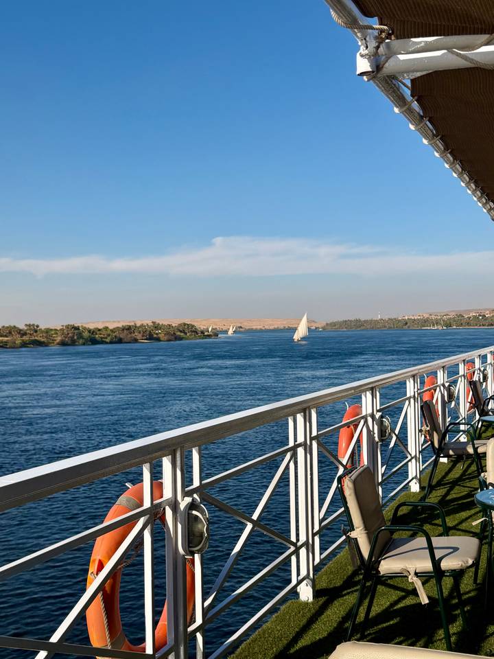 Serene view from cruise deck over wide blue Nile with traditional white-sailed feluccas catching the breeze.