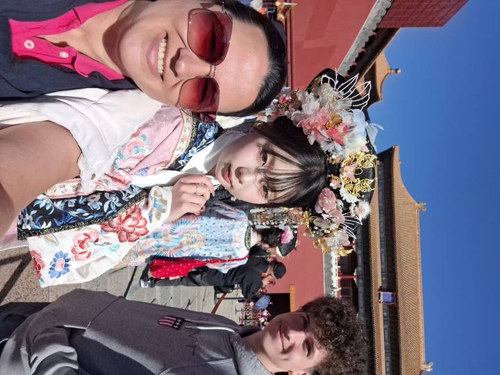 Travellers with a woman in ornate traditional dress inside the Forbidden City courtyard on a sunny day.