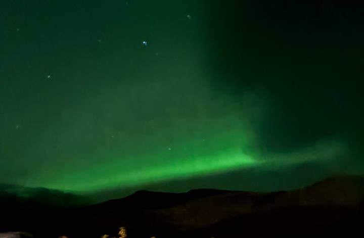 Soft green aurora borealis glowing above dark mountain silhouettes in the night sky.