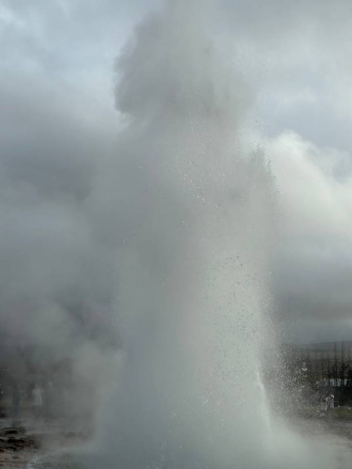 Close-up of a geyser eruption with a dense column of steam against a gray sky.