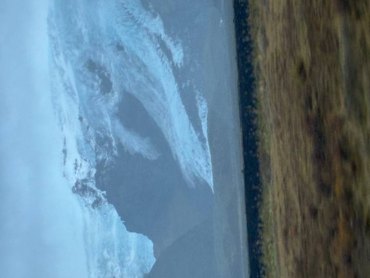 Blurry view of a glacier-covered mountain taken from a moving vehicle on an overcast day.