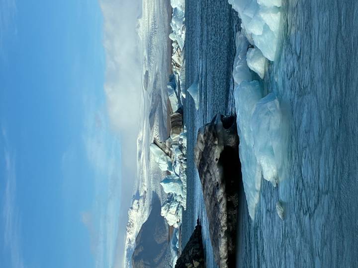 Bright blue lagoon filled with floating icebergs under a clear sky.