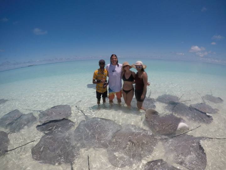 Small group posing in knee-deep water among many stingrays with a vast turquoise lagoon behind.