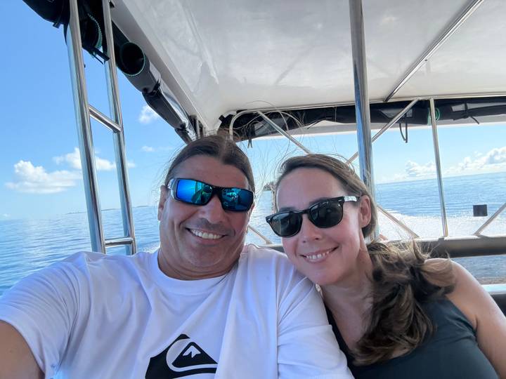 Smiling couple take a selfie on a speedboat with sparkling blue water behind.