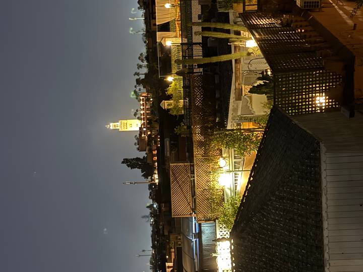 Nighttime rooftop view of Marrakesh with a lit minaret rising above garden terraces.