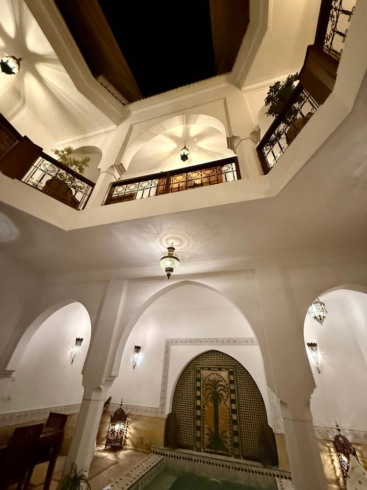 White arched interior of a traditional riad with ornate metal lantern lighting.
