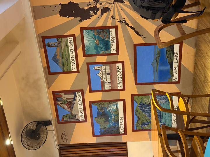 Cafe wall decorated with illustrated panels of popular Philippine destinations and wooden chairs in the foreground.