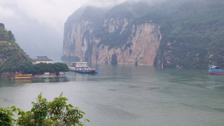 Foggy gorge with towering limestone cliffs and cruise vessels moored along the river.