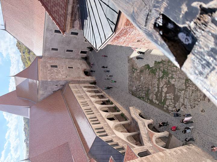 Bird’s-eye view into a stone courtyard of a Gothic castle complex with visitors walking below.