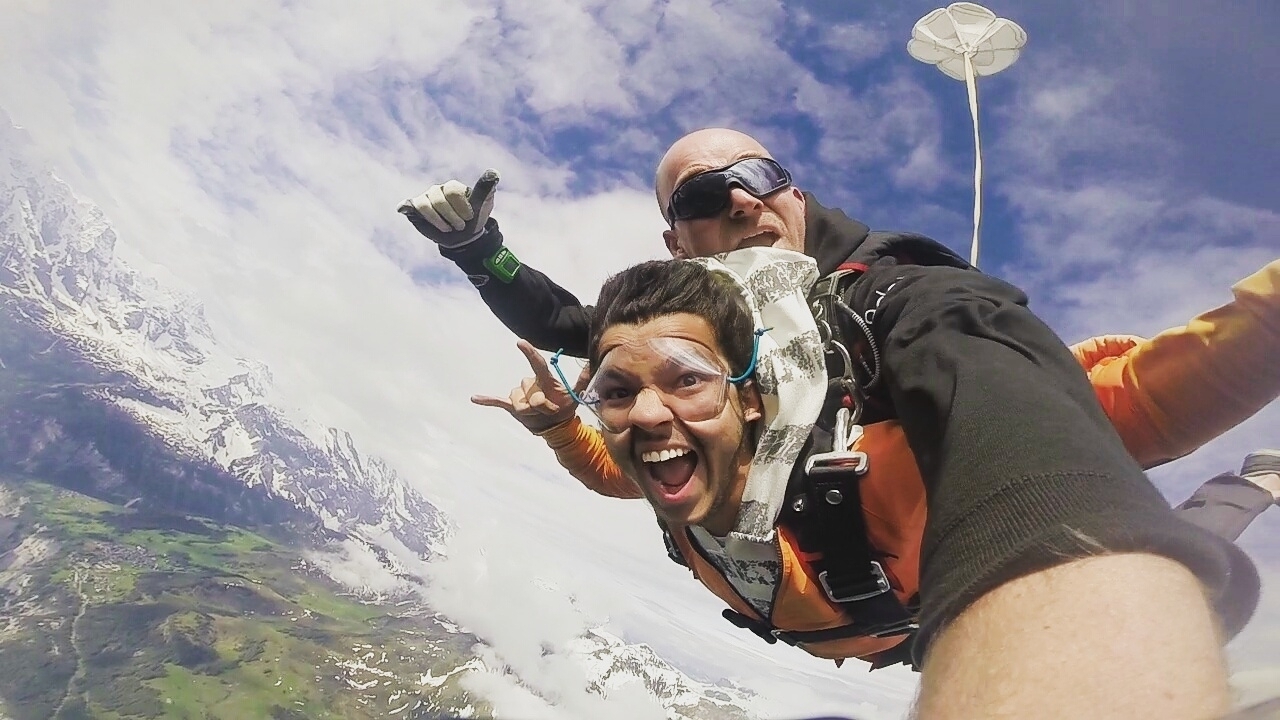 Two people skydiving with mountains and sky in the background.