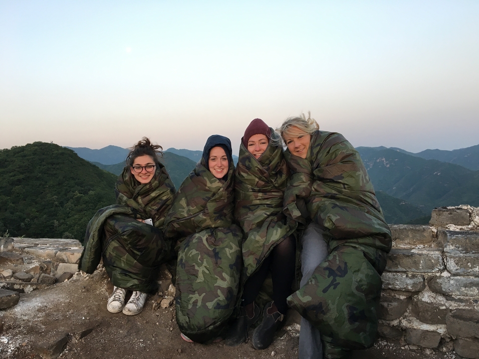 Groupe de personnes enveloppées dans des couvertures sur un mur à l'aube.