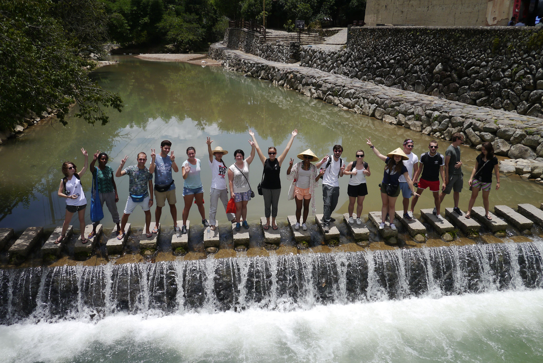Ligne de personnes se tenant sur un petit pont enjambant un ruisseau.