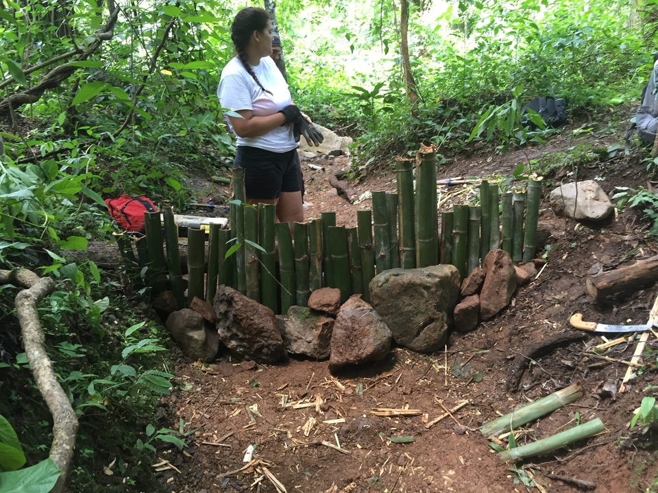 Person working with bamboo and stones in a jungle setting.