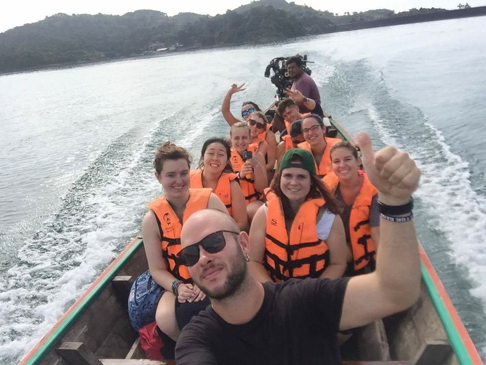 Group of people wearing life jackets on a boat with one giving a thumbs-up.