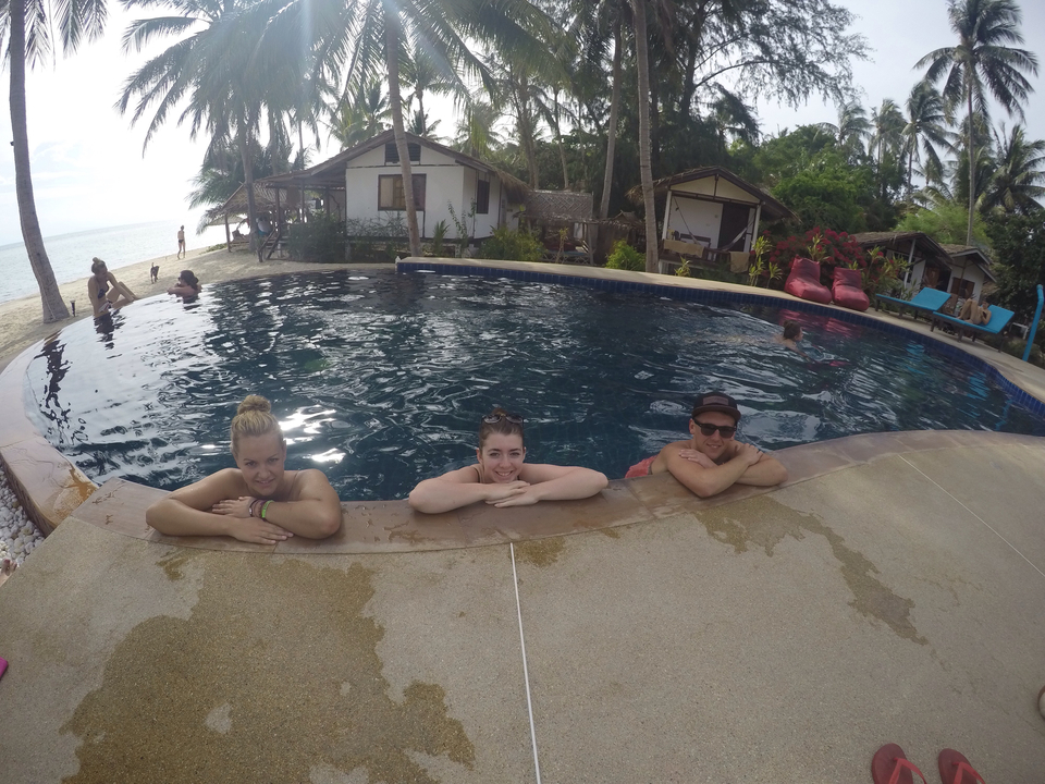 Friends relaxing in a pool with huts and palm trees.