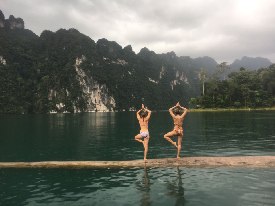 Two people doing yoga poses on a log in a lake with mountains in the background.