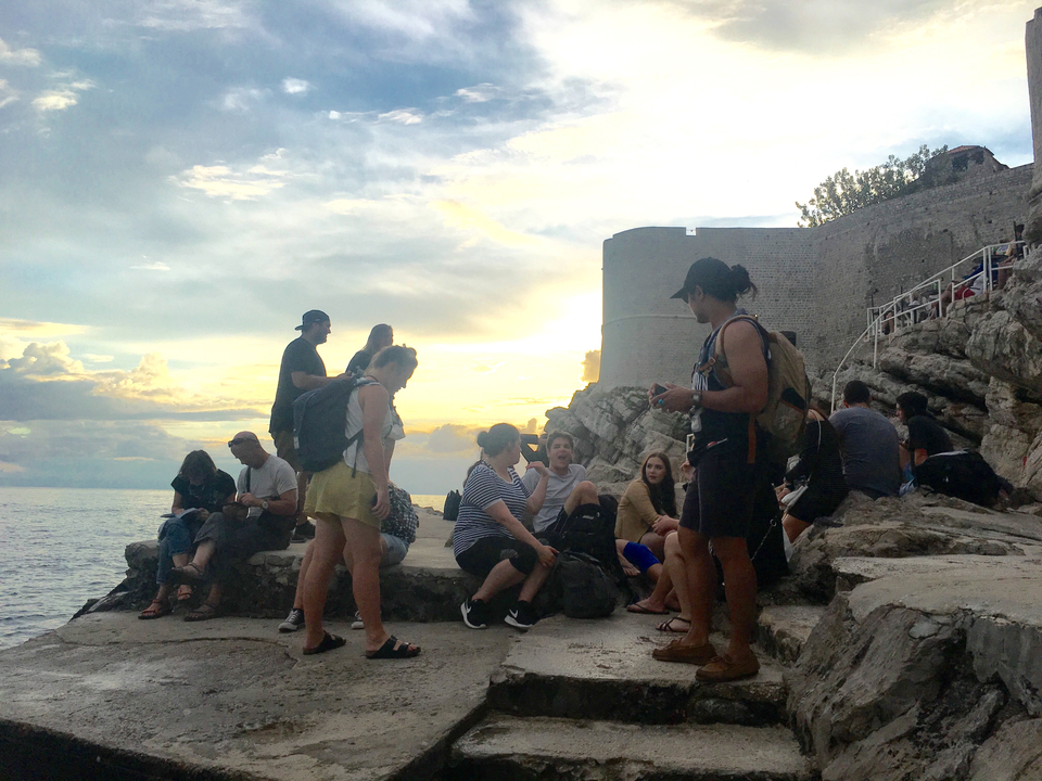 People gathering on rocks by the sea with a sunset in the background.